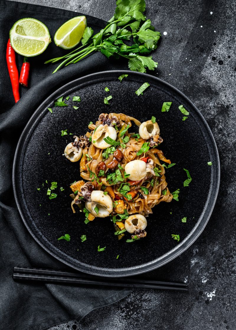 homemade-stir-fry-damage-noodles-with-seafood-and-vegetables-in-a-plate-black-background-top-view.jpg
